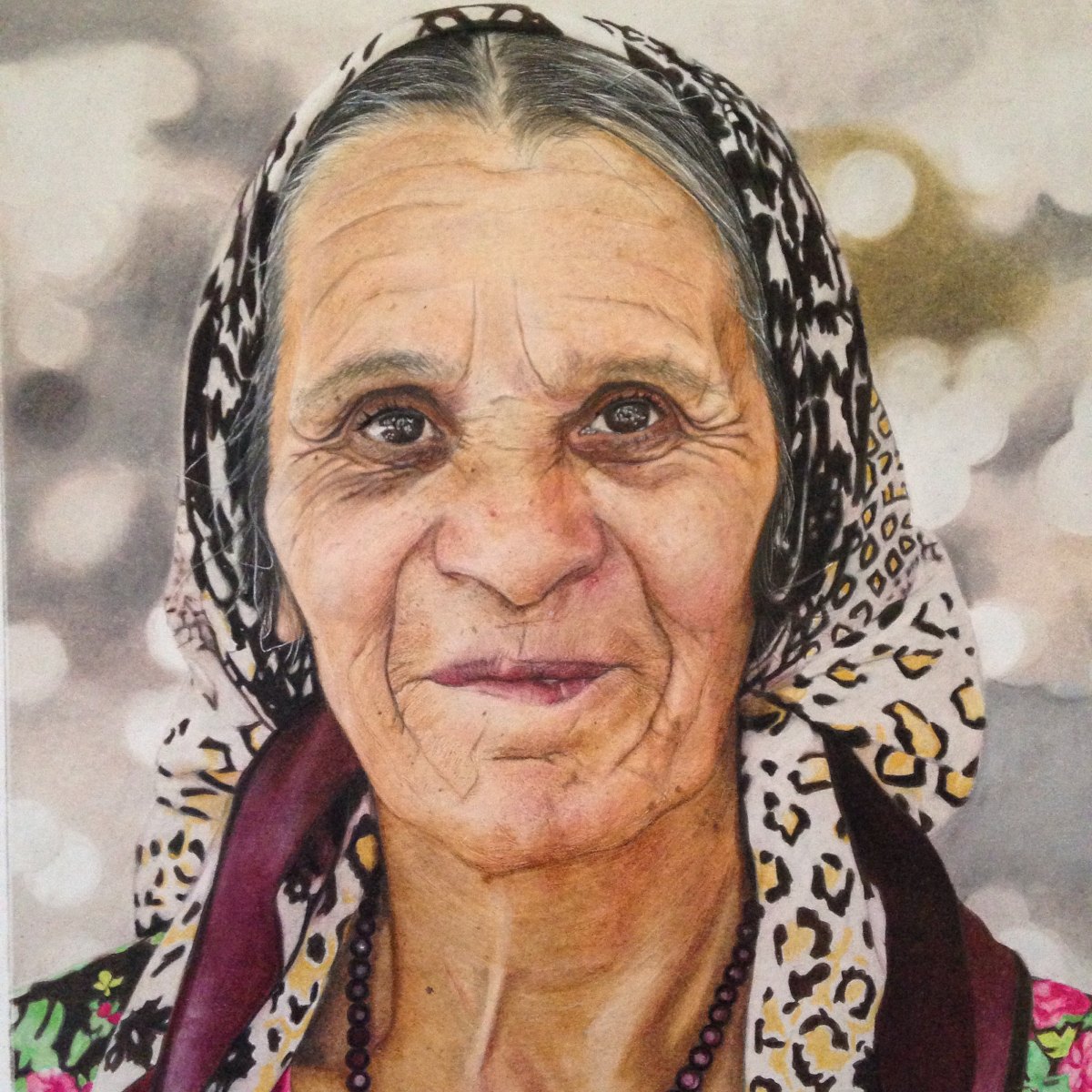 Oil based colour pencil portrait on smooth surface paperPortrait of a Romanian elderly woman with grey hair, smiling gently, wearing a patterned headscarf and a beaded necklace, against a blurred background. By fine artist Andreea Ionela Berindei